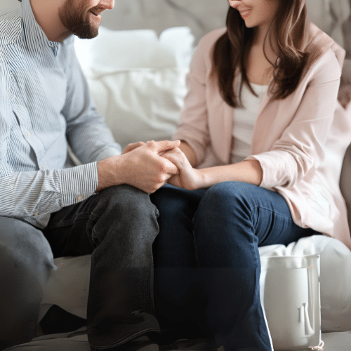 Man and women sitting on sofa clasping hands